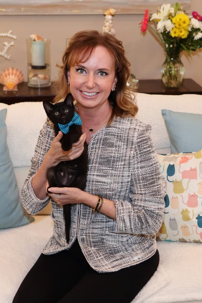 a cat rescue photographer sitting on the couch holding a black kitten that is up for adoption.